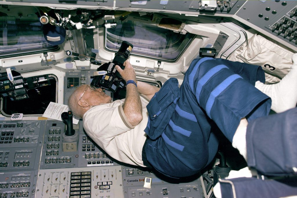 Astronaut and U.S. Senator John Glenn positions himself to take photos from the Discovery’s aft flight deck windows on October 30, 1998. 